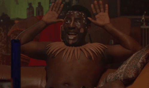 a shirtless man with a necklace around his neck is smiling with his hands in the air