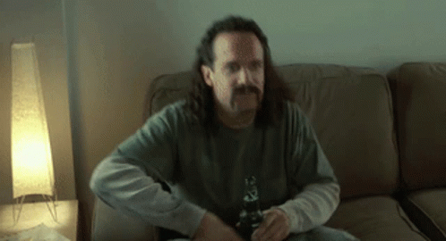 a man with long hair is sitting on a couch holding a beer bottle